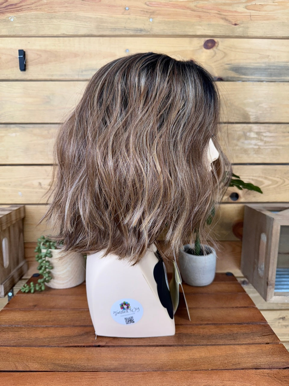 Mannequin head with a wig on a wooden table against a wooden wall.