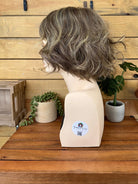 Mannequin head with a gray wig on a wooden surface with a wooden wall background