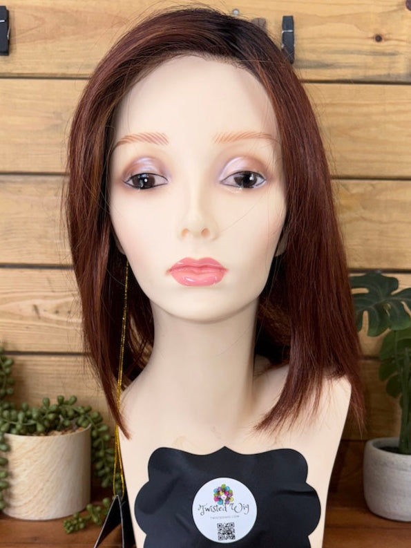 Mannequin head with brown hair on a wooden stand against a wooden wall.