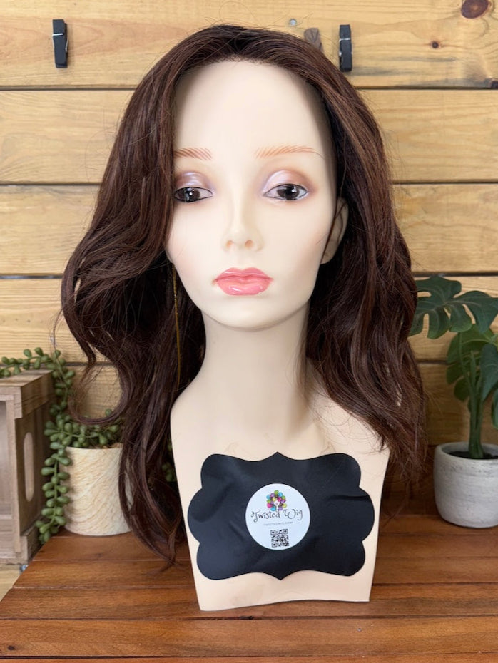 Mannequin head with a brown wig on a wooden table against a wooden wall.