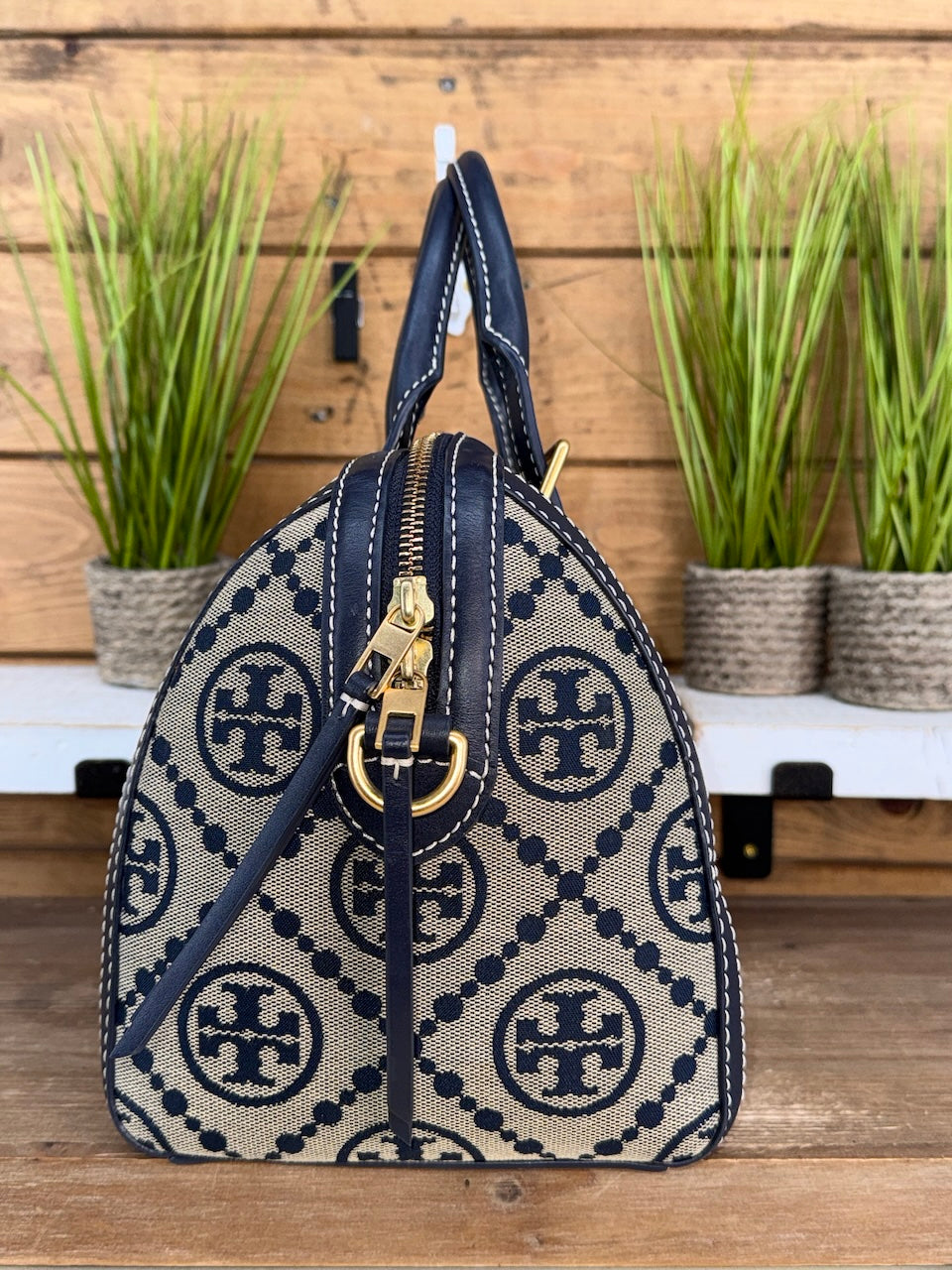 Handbag with a patterned design on a wooden surface with plants in the background