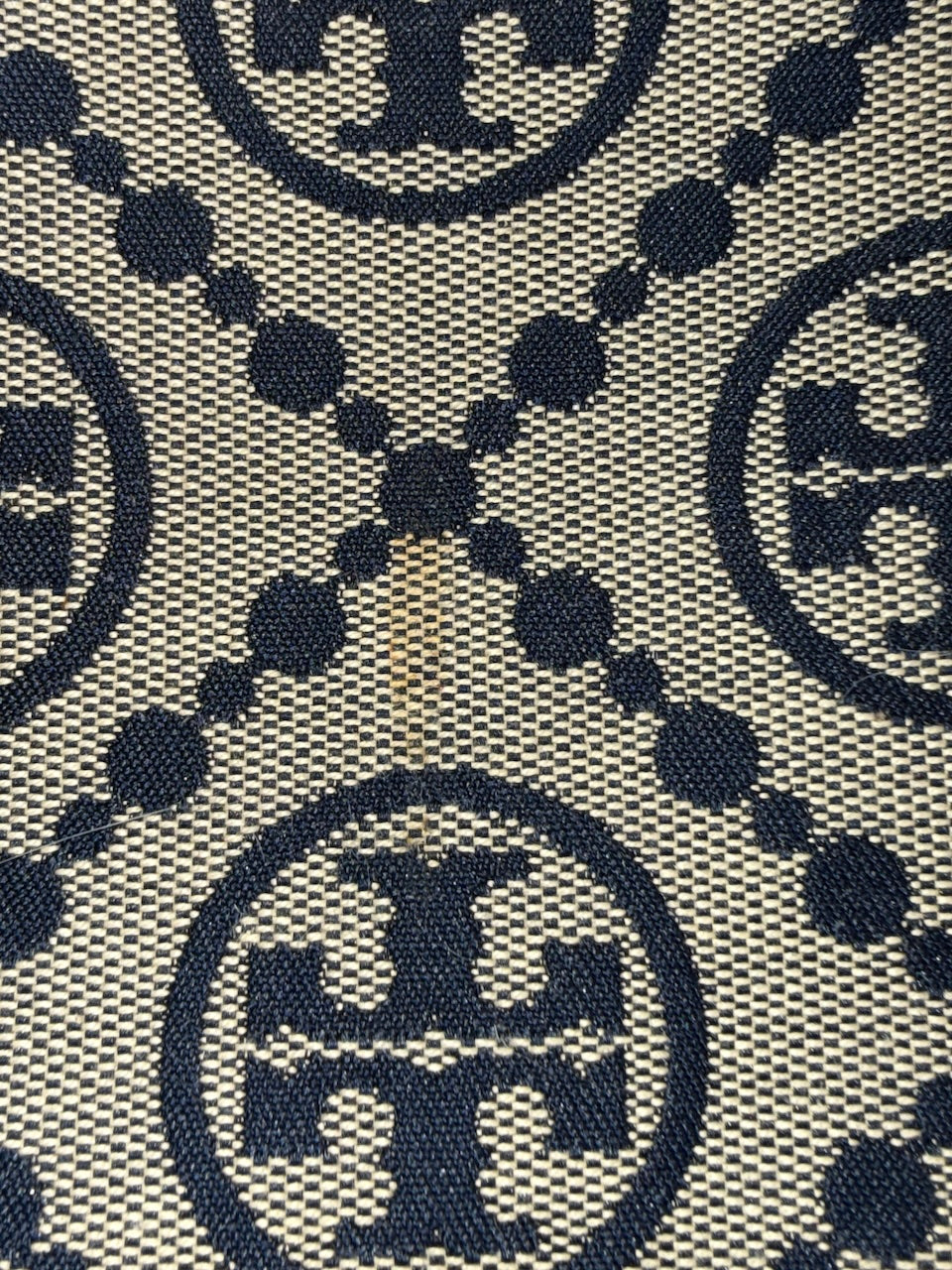 Close-up of a patterned fabric with repeated logo design - showing slight discoloration in fabric